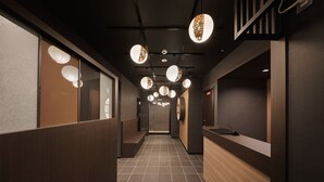 Un pasillo moderno de hotel con un mostrador de recepción de madera, suelo de baldosas y farolillos de papel colgantes.