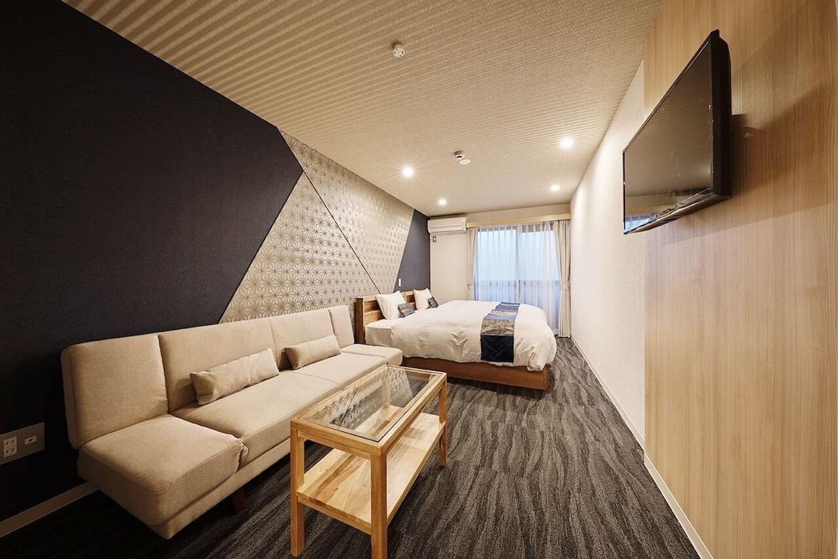 Una habitación de hotel con sofá, cama, televisión y suelo alfombrado.