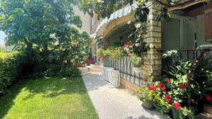 A well-maintained garden with a stone pathway leading to a house with a tiled roof and a metal railing. - Holiday apartment with garden and terrace (Rovinj)