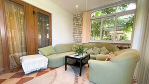 A living room with a sofa, a coffee table, and a large window with a view of trees. - Holiday apartment with garden and terrace (Rovinj)