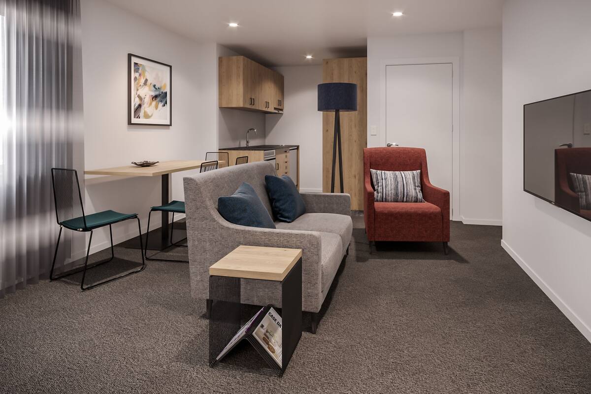 A modern living room with a grey sofa, a red armchair, a small table, and a kitchen area in the background.