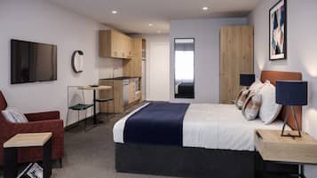 Una habitación de hotel moderna con cama, escritorio, silla, televisor, kitchenette y un ventanal amplio.