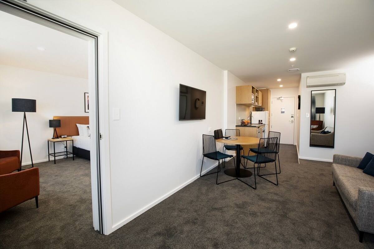 A modern hotel room with a dining area, a sofa, and a TV.