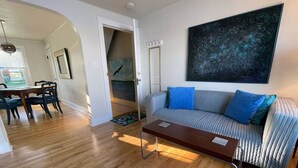 Un salon avec un plancher en bois, un canapé avec des coussins bleus, une table basse et un tableau accroché au mur.