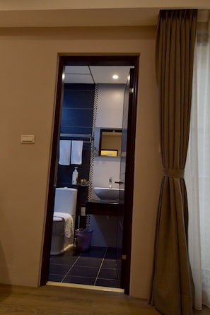 A hotel room with a dark-colored door, a visible bathroom with a sink and toilet, and a curtain on the right side. - The 123 B&B (Ji'an)