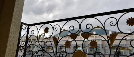 Varanda com guarda-corrimão de metal com detalhes florais, um parapeito de pedra e vista para um edifício com várias janelas e varandas.