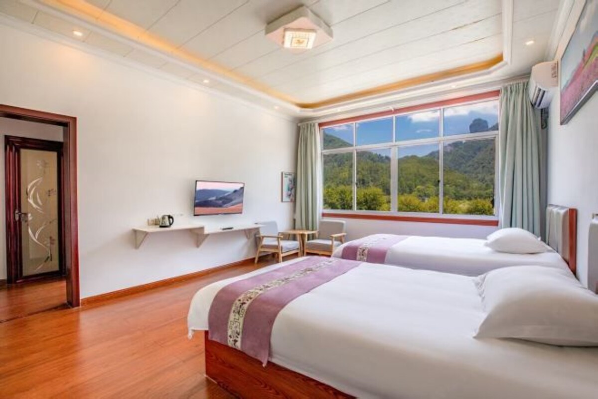 Habitación de hotel con dos camas, un escritorio, una silla, un televisor y un amplio ventanal con vistas a la montaña.