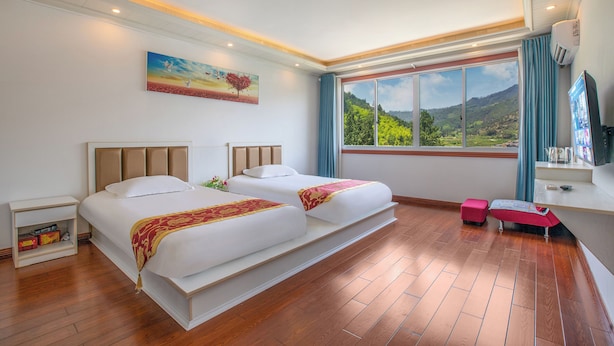 A hotel room with two beds, a large window with a mountain view, a painting on the wall, and a small desk with a TV. - Lv ye Xian Zhuang Guesthouse (Taizhou)