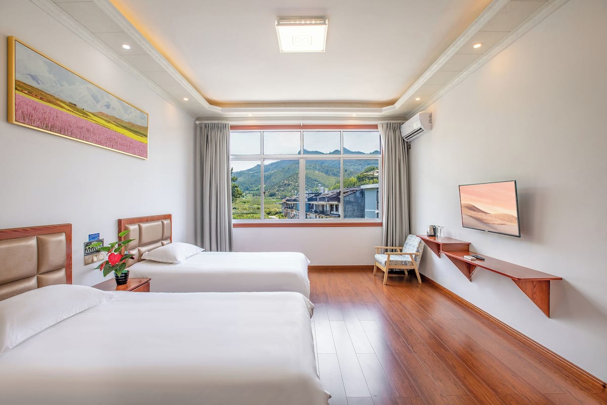 A hotel room with two beds, a desk, a chair, a TV, and a window with a mountain view.