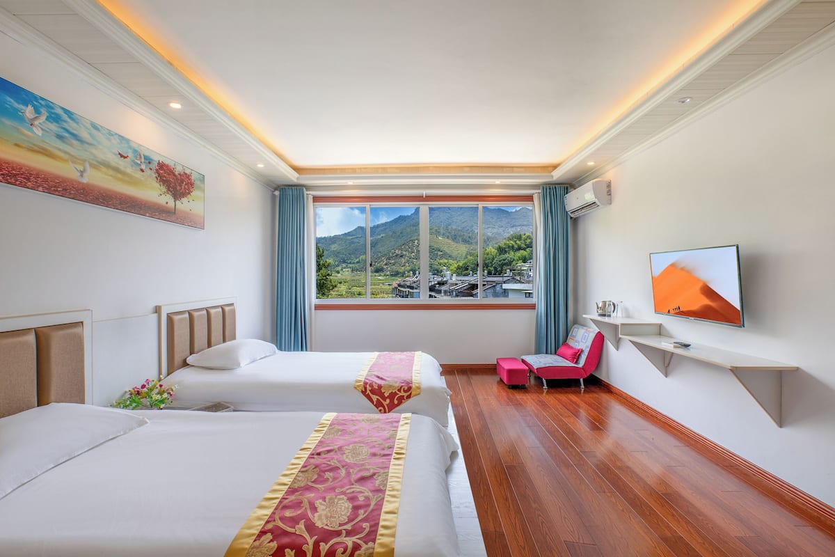 A hotel room with two beds, a TV, a desk, and a window with a mountain view.