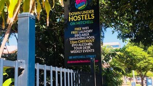 Skilt for Down Under Hostels på Mitchell Street, der reklamerer for faciliteter som gratis WiFi, vaskeri, grillområde, swimmingpool og ugentlige arrangementer.