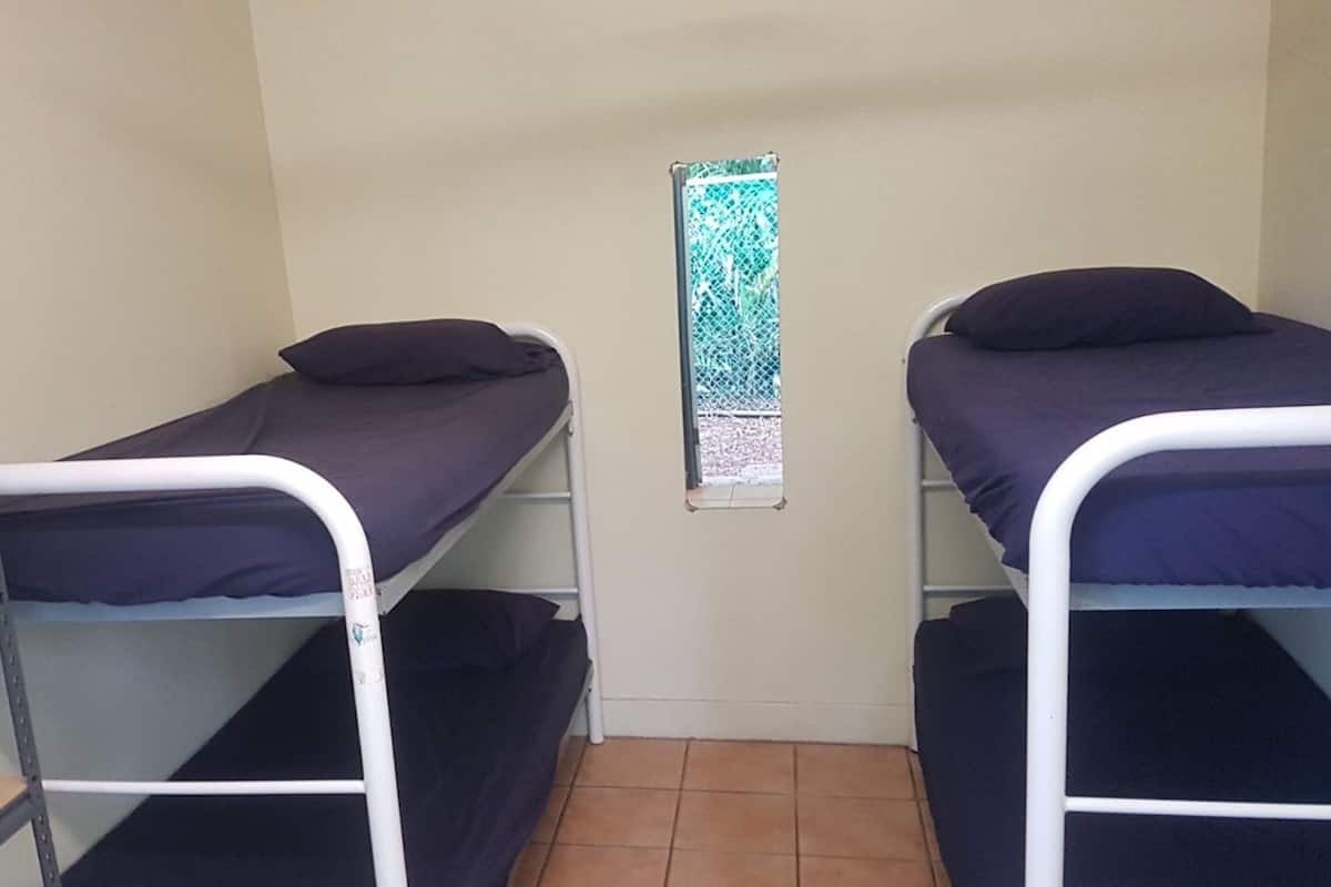 A dormitory room with two bunk beds, a metal desk, and a window with a decorative screen.