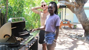 En person griller udendørs ved en grill, med et picnicbord i baggrunden.