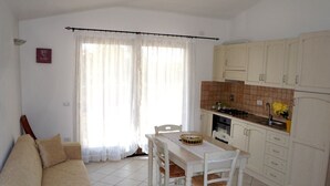 A living room with a sofa, a dining table with chairs, and a kitchen area with cabinets and a stove. - Sardinia-Pittulongu-Holiday home w/ garden 5 min. walk from withe sandy beaches (Olbia)