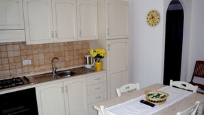 A kitchen with white cabinets, a sink, and a stove. There is a dining table with chairs and a vase of flowers. - Sardinia-Pittulongu-Holiday home w/ garden 5 min. walk from withe sandy beaches (Olbia)
