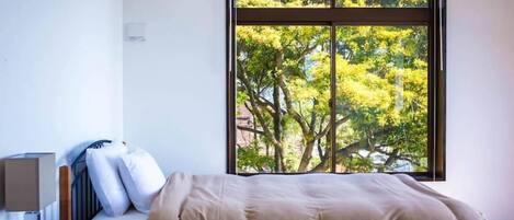 Un dormitorio con una ventana grande, una cama, una mesita de noche y una lámpara.