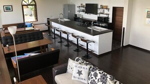 A modern kitchen with a central island, bar stools, and a dining area with a sofa and table. - The Little Garden (Miyazaki)
