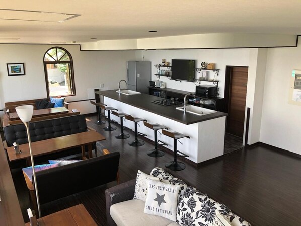 A modern kitchen with a central island, bar stools, and a dining area with a sofa and table. - The Little Garden (Miyazaki)