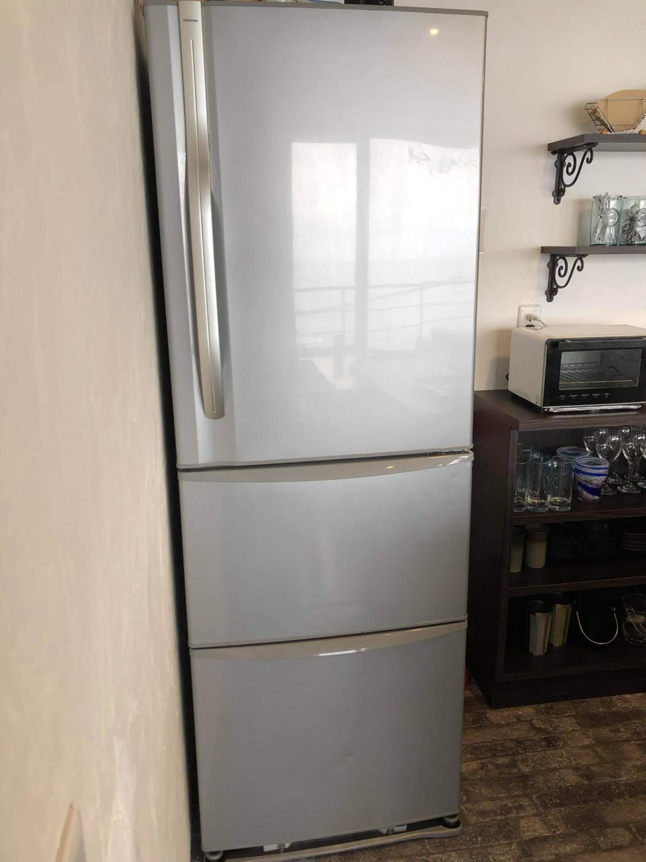 Una cocina compacta con un refrigerador de acero inoxidable, un microondas y una alacena con cristalería.