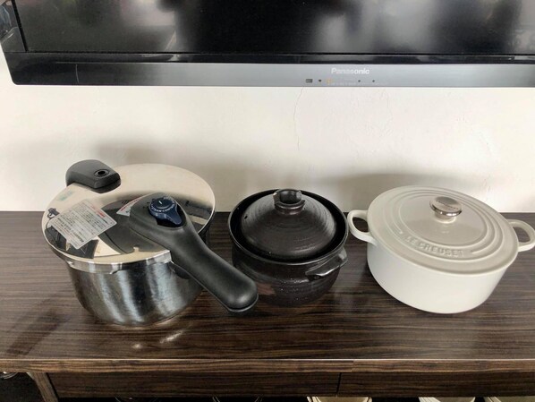 Una encimera de cocina con una olla de acero inoxidable, una olla negra con tapa y una olla de cerámica blanca con tapa.