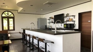 A modern kitchen with a central island, bar stools, a flat-screen TV, and a large window. - The Little Garden (Miyazaki)