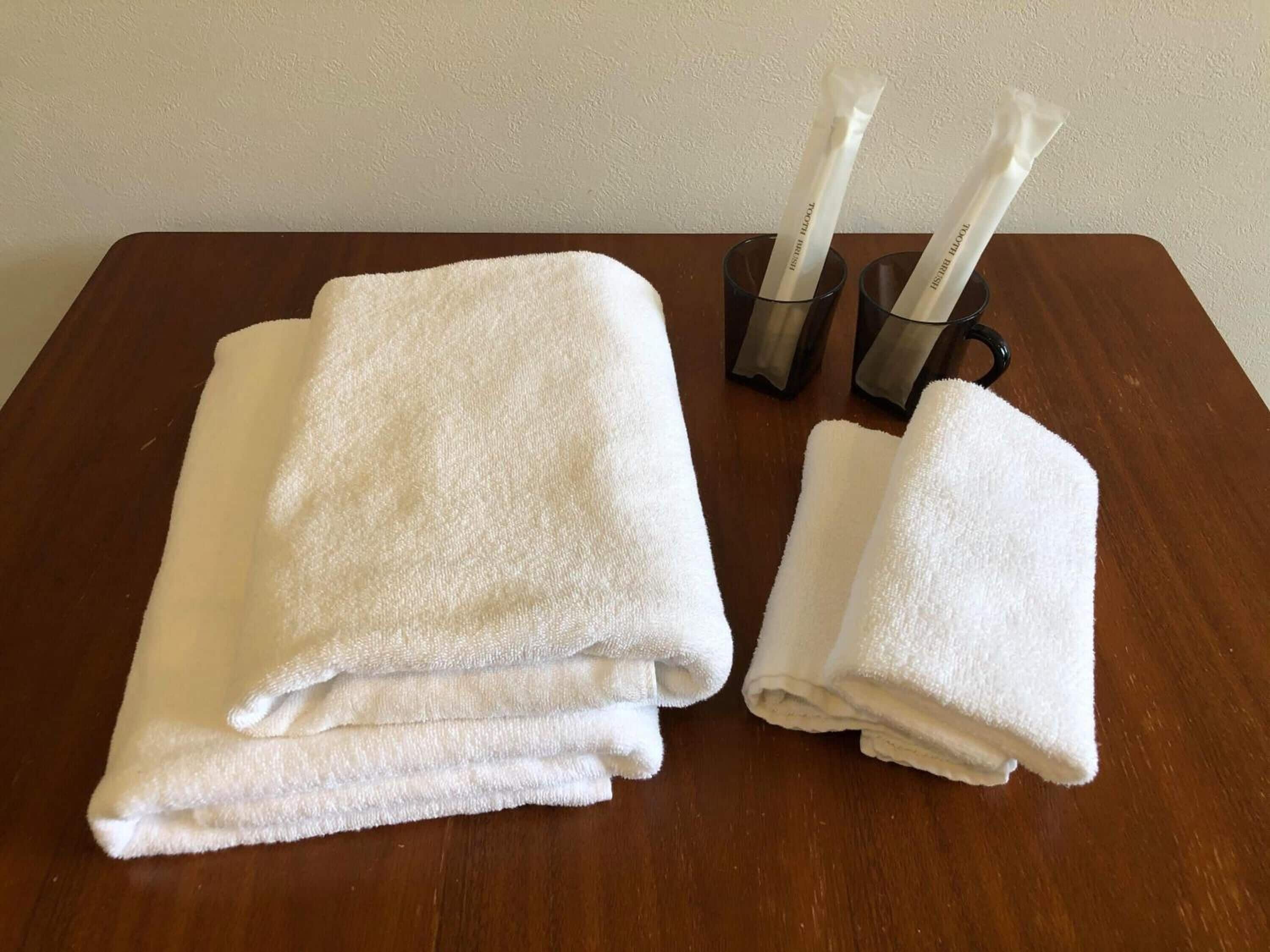 A wooden table with two neatly folded white towels and a pair of black-handled glass containers with white straws.