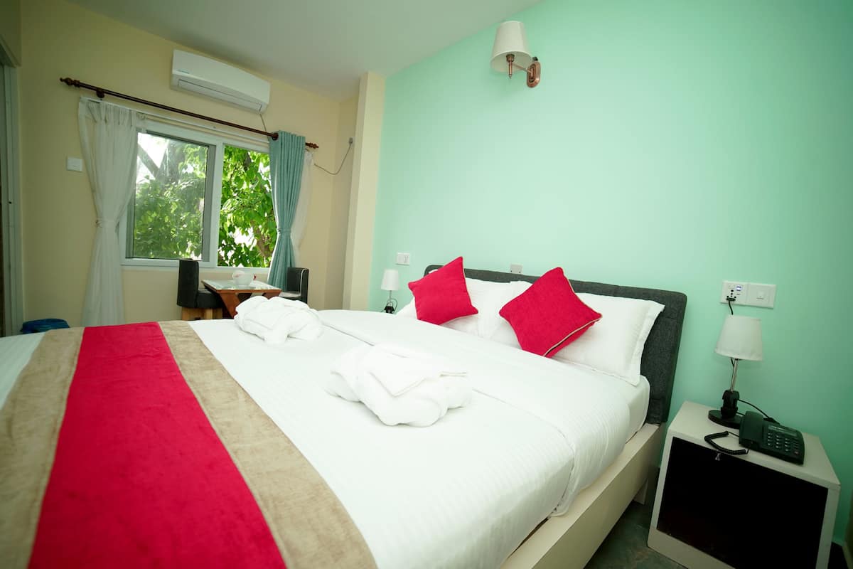 A hotel room with a large bed, two bedside tables, a desk, and a window with curtains.
