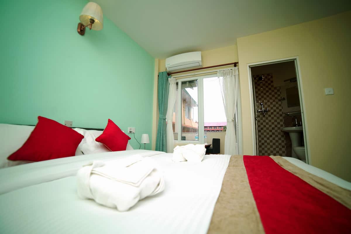 A hotel room with a bed, red pillows, a white blanket, and a red and beige bedspread.