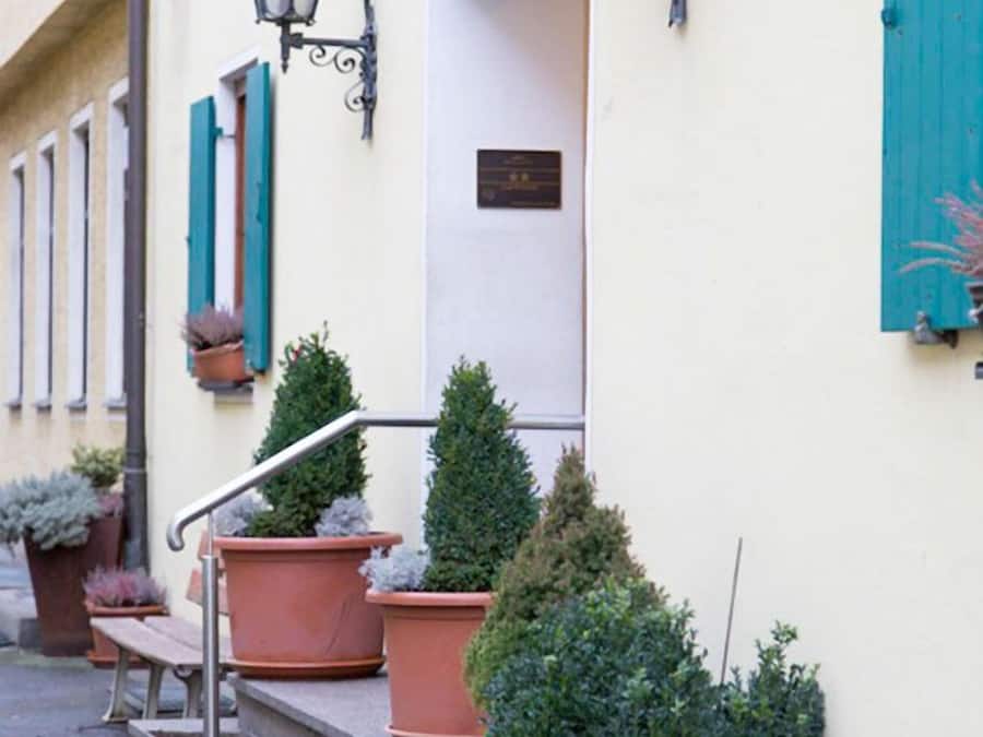 A building with a white facade, terracotta potted plants, and a metal staircase leading to a door.
