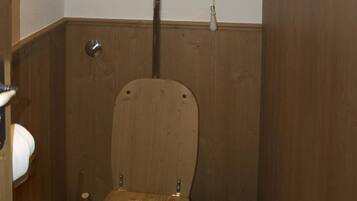 Baño pequeño con piso de madera, un inodoro, un balde de madera y un dispensador de papel higiénico.