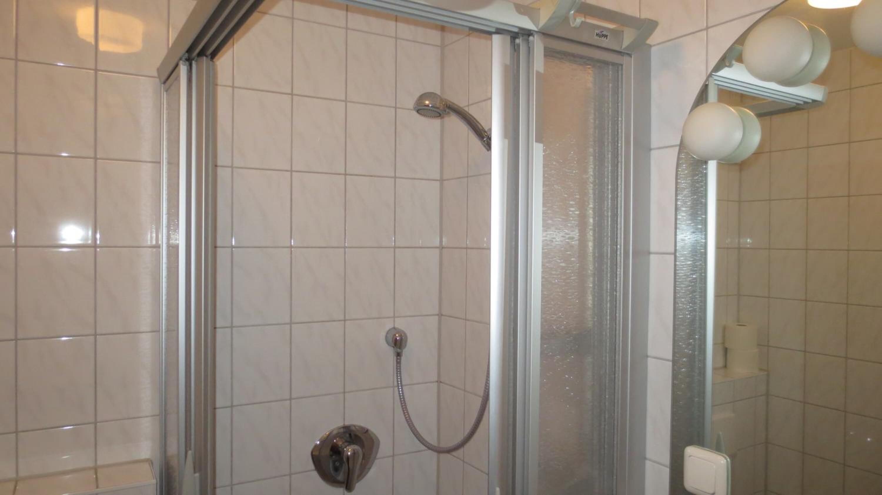 A glass-enclosed shower with a handheld showerhead and a wall-mounted faucet.