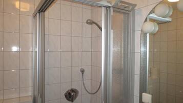 A glass-enclosed shower with a handheld showerhead and a wall-mounted faucet.