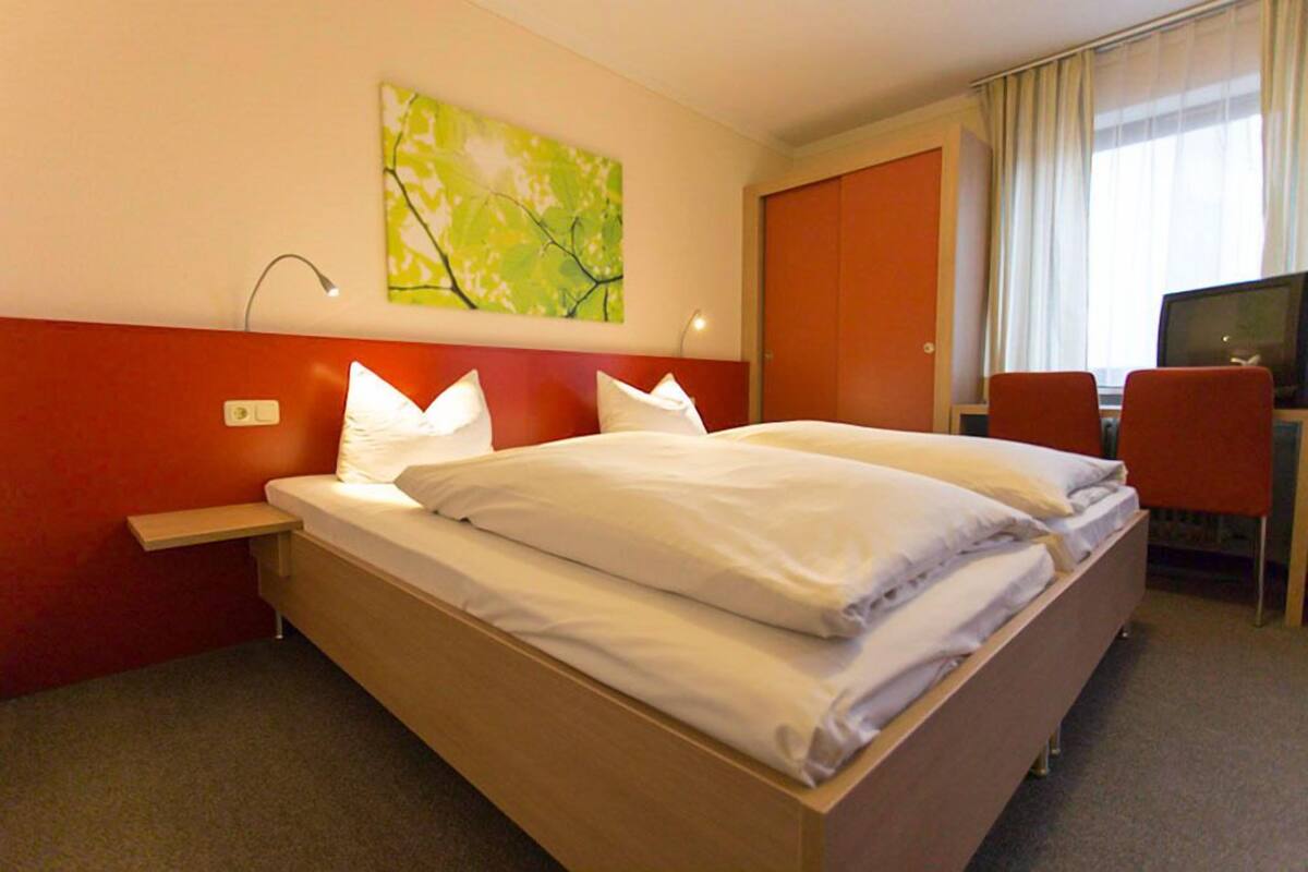 Een hotelkamer met een tweepersoonsbed, een bureau met stoel, een televisie en een schilderij aan de muur.