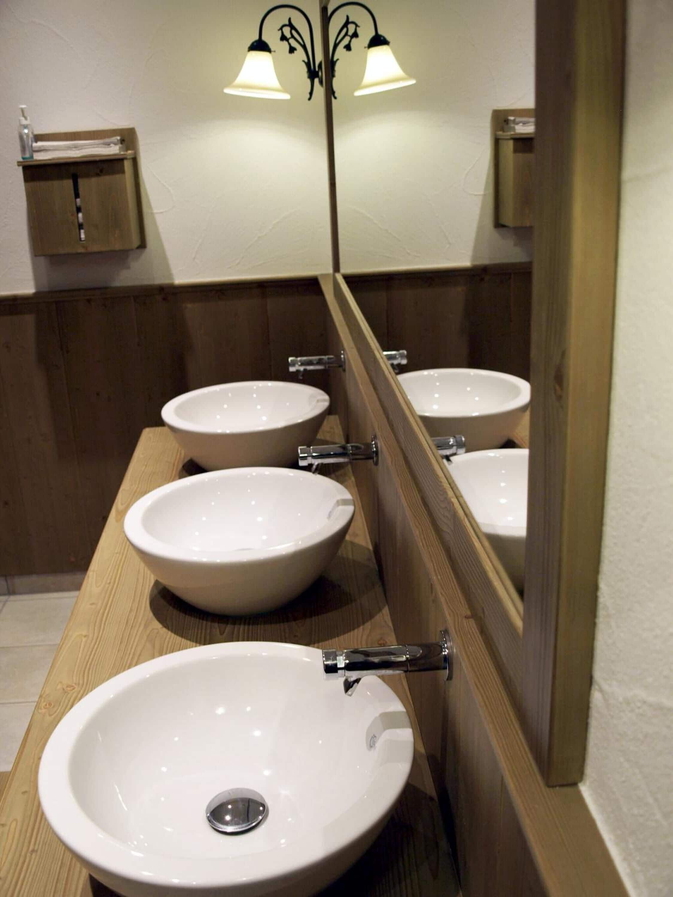 Un baño con tres lavamanos blancos y un espejo.