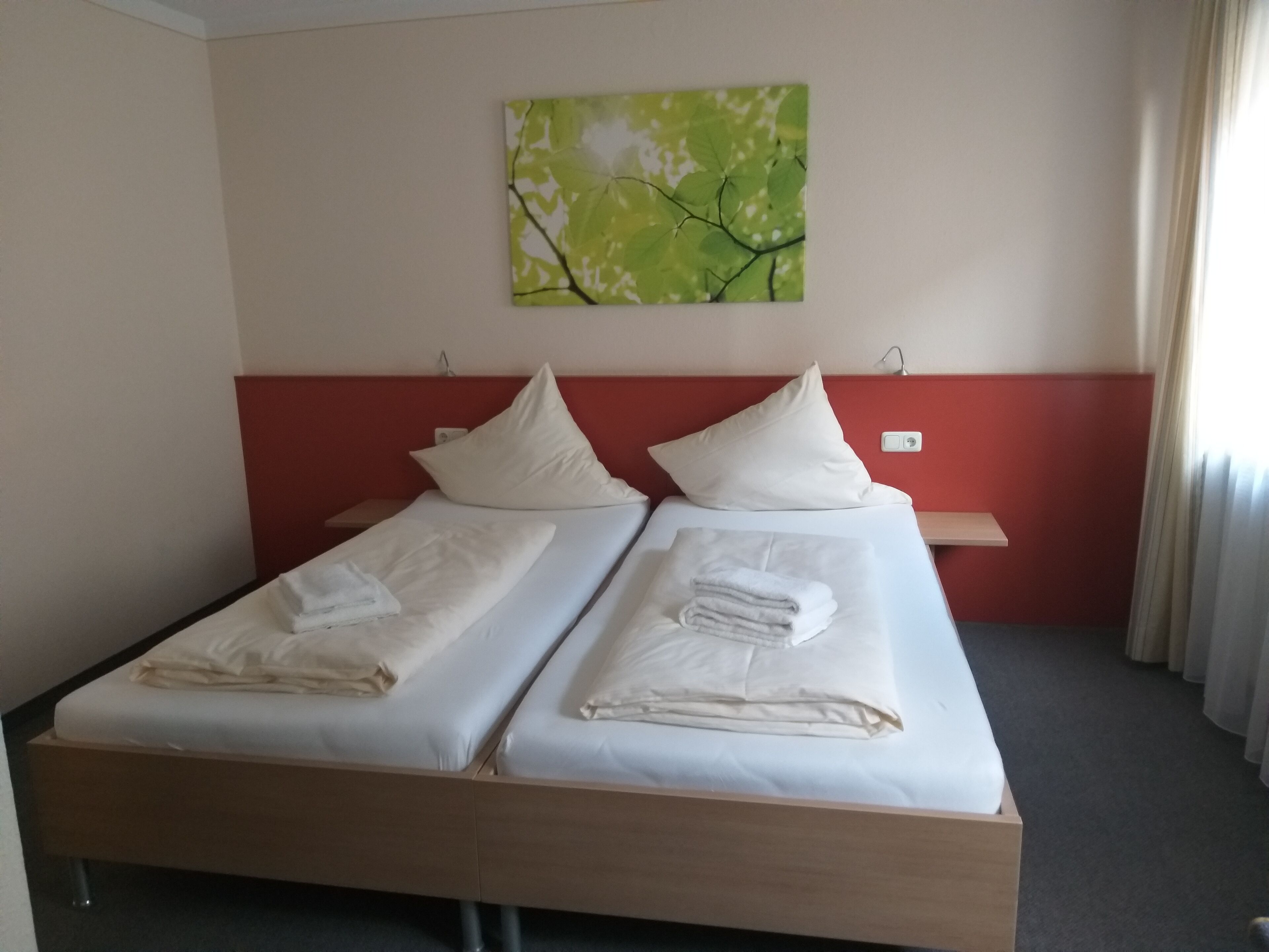Una cama doble con ropa de cama y almohadas blancas, una mesita de noche pequeña, un cabecero rojo y un cuadro colgado en la pared.