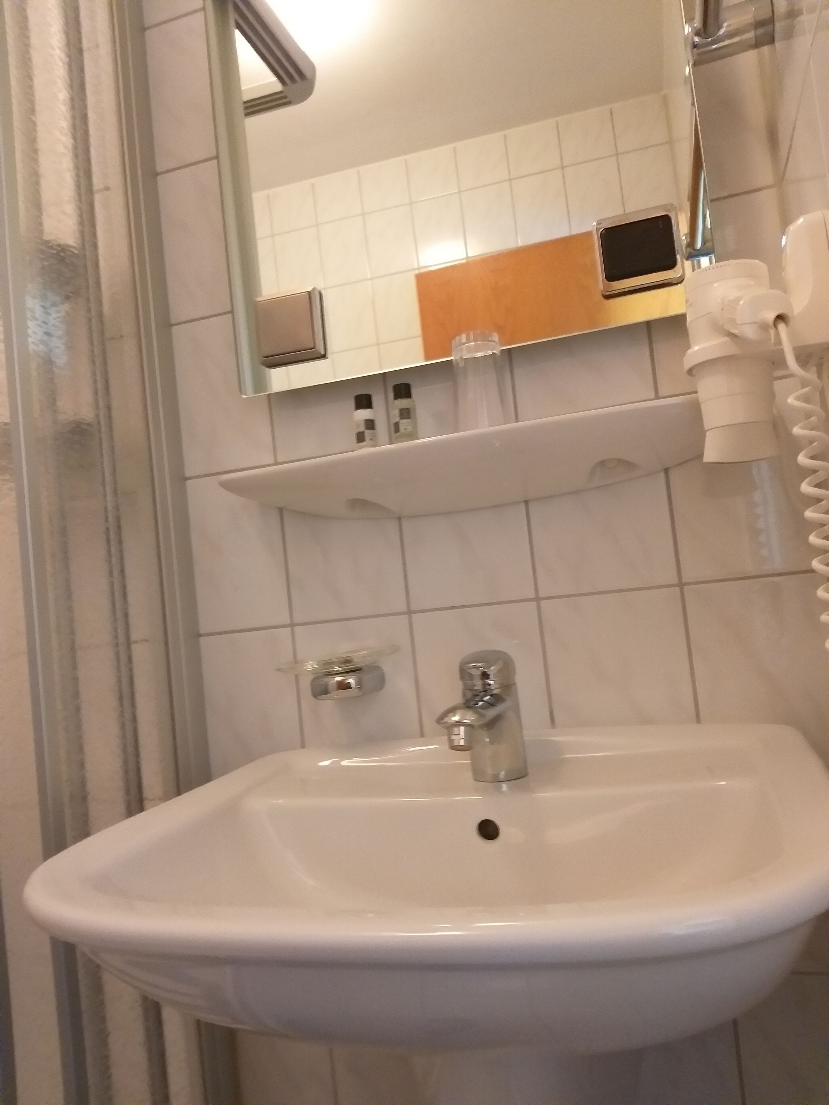 Een badkamer met een witte wastafel, een spiegel, een handdoekrek en een douche.
