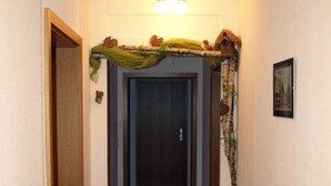 Un couloir au sol en bois, une porte sombre au fond et un luminaire au plafond.