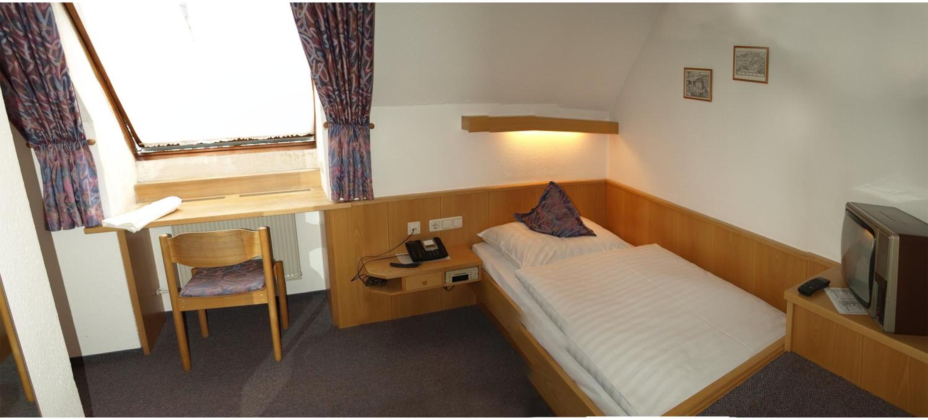 A compact hotel room with a single bed, a desk with a chair, a television, and a small table.