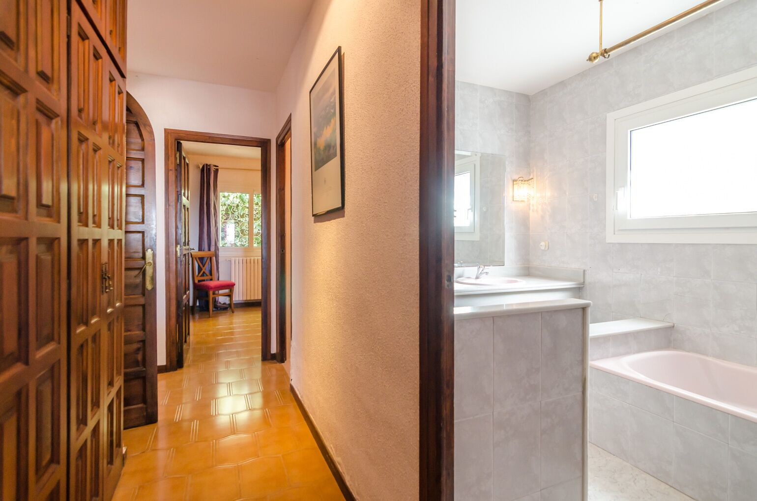 Un pasillo que conduce a un baño con una bañera, un lavamanos y una silla.