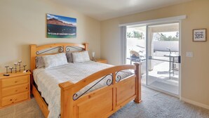 A bedroom with a wooden bed, a nightstand, a ceiling fan, a painting, and a sliding glass door leading to an outdoor area. - Pool, Hot Tub & Mtn Views: Lake Havasu City Home! (Lake Havasu City)