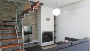 A modern living room with a grey sofa, a fireplace, a TV mounted on a stone wall, and a staircase with wooden steps.