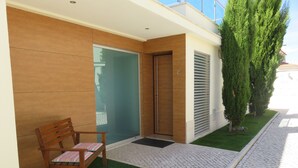 A modern building with a wooden exterior, a glass door, and a small outdoor seating area with a chair.