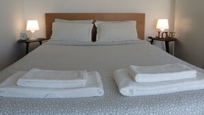 A neatly made bed with a patterned bedspread, two pillows, and two bedside tables with lamps and a clock on one side.
