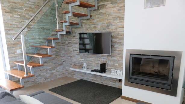 A modern living room with a stone wall, a staircase, a flat-screen TV, a fireplace, and a sofa.