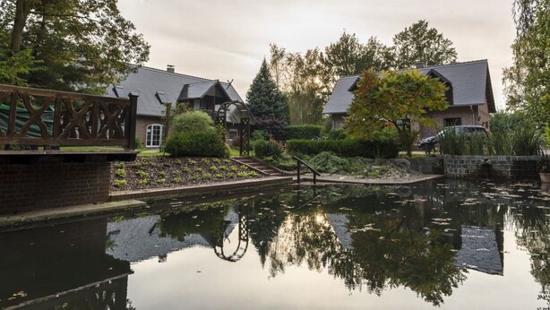 Ein friedlicher Innenhof mit Teich, Backsteinwegen und Gebäuden im traditionellen Stil mit geneigten Dächern.