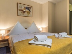 A hotel room with a bed, pillows, a yellow blanket, and a rolled towel on the bed.