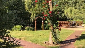 Ein Gartenweg führt zu einer Holzhütte mit roten Blüten.