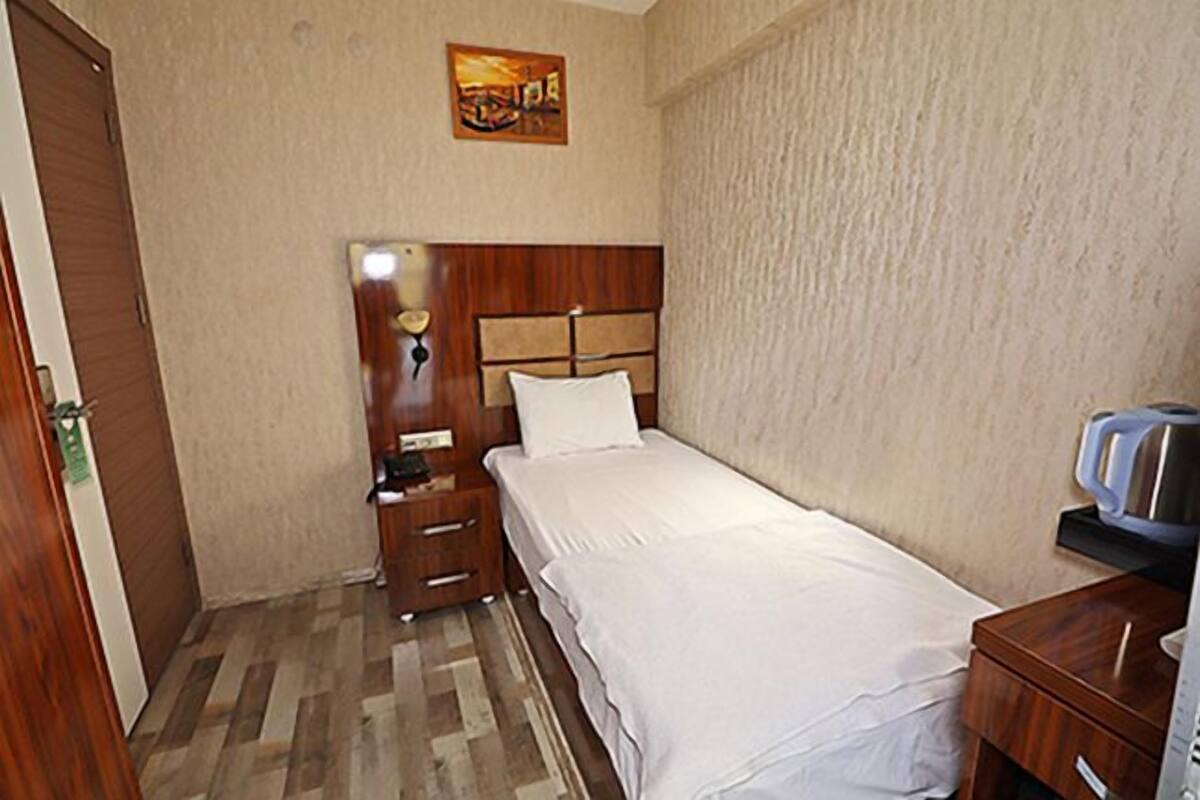 A hotel room with a wooden headboard bed, a bedside table with a lamp, a small cabinet, and a painting on the wall.