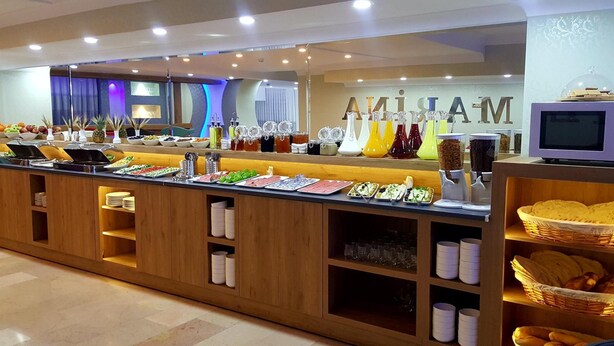 A buffet counter with various food items and condiments, wooden cabinets, and a television screen. - Marina Hotel (Izmir)