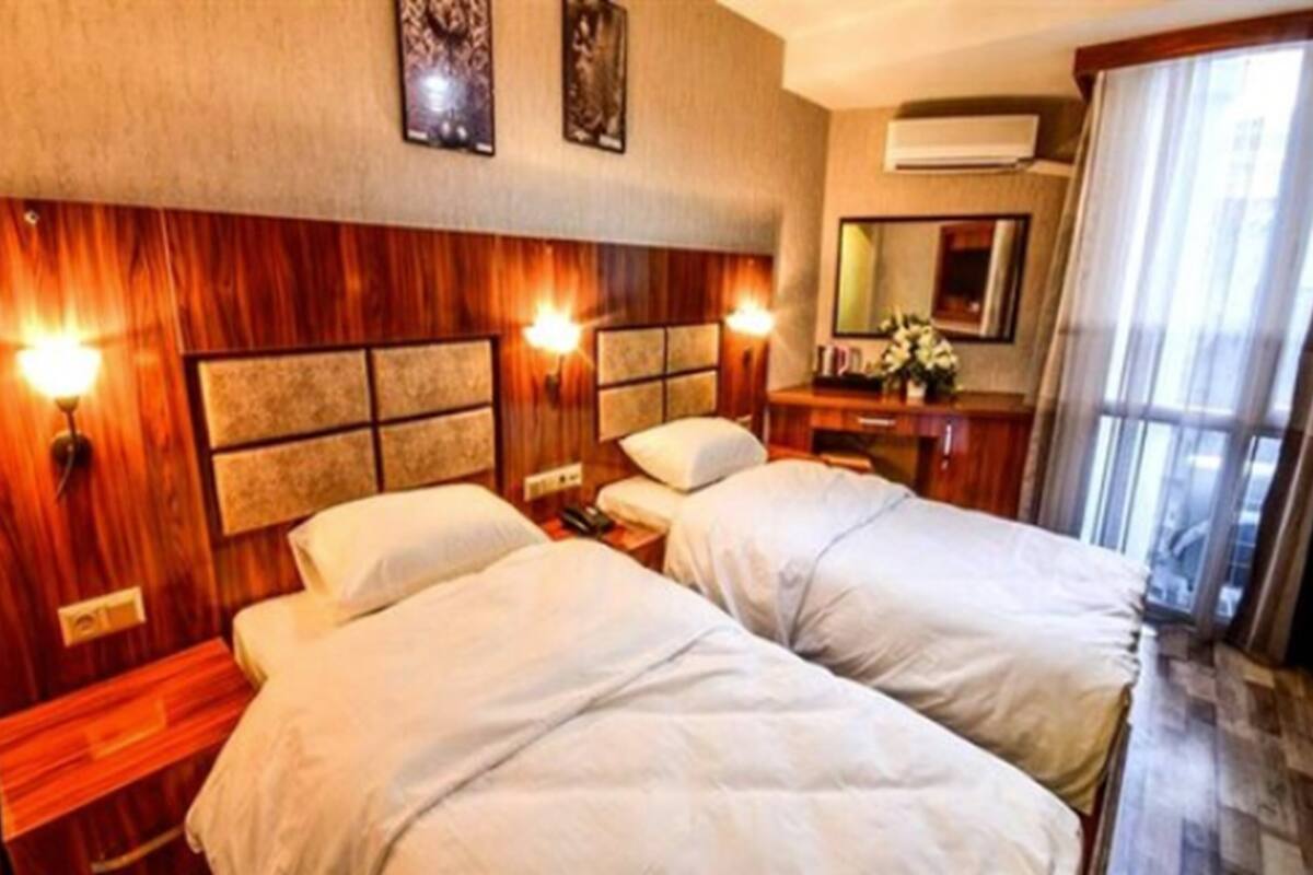 A hotel room with two beds, wooden headboard, bedside lamps, a mirror, and a window with curtains.